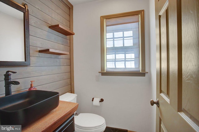 bathroom with vanity, toilet, and wood walls