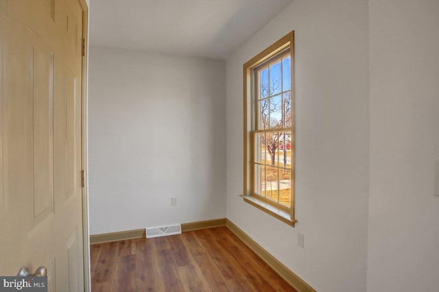 spare room featuring dark wood-style floors, visible vents, a healthy amount of sunlight, and baseboards