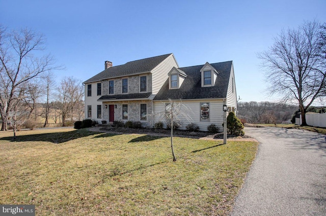 view of front of home featuring a front yard, stone siding, driveway, and a chimney