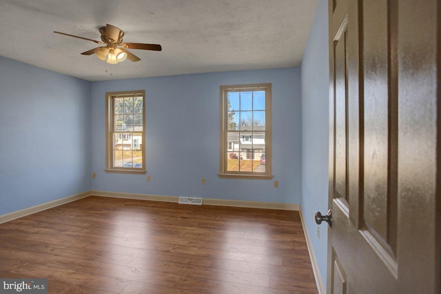 empty room with visible vents, a ceiling fan, baseboards, and hardwood / wood-style flooring