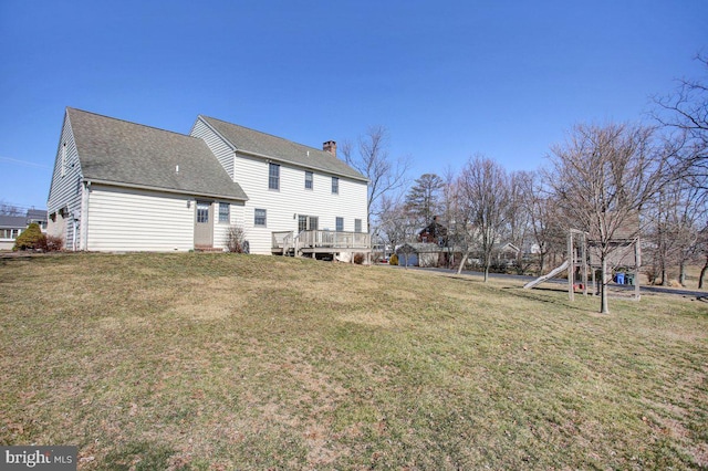 back of house with a chimney, a yard, and a shingled roof