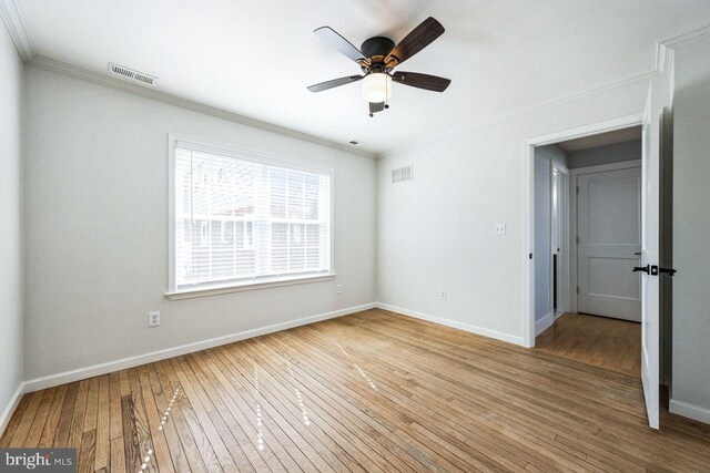 empty room featuring baseboards, visible vents, light wood finished floors, and ornamental molding