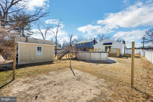 view of yard featuring a deck, a covered pool, a fenced backyard, an outdoor structure, and stairs