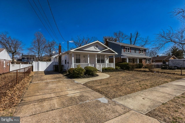 view of front facade featuring a gate, fence, a porch, a chimney, and concrete driveway