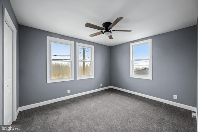 unfurnished room with dark colored carpet, a ceiling fan, and baseboards