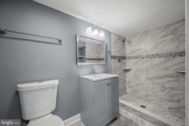 bathroom with marble finish floor, tiled shower, vanity, and toilet