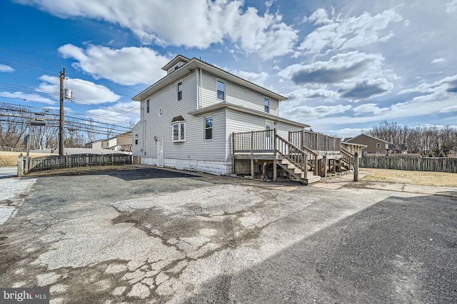 view of side of home with stairs, aphalt driveway, fence, and a deck