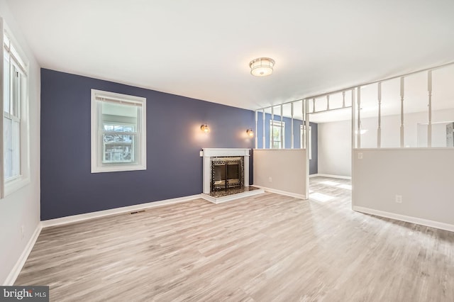 unfurnished living room with baseboards, visible vents, a fireplace with raised hearth, and wood finished floors