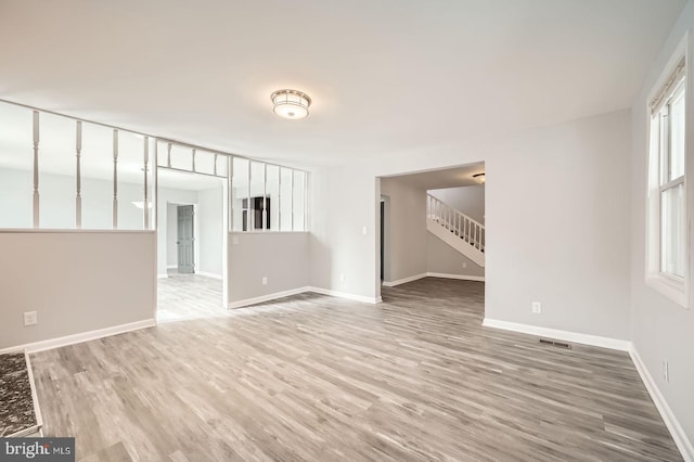 empty room featuring visible vents, stairway, baseboards, and wood finished floors