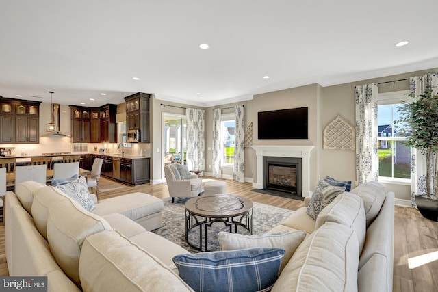 living area with recessed lighting, a fireplace with flush hearth, light wood finished floors, and baseboards