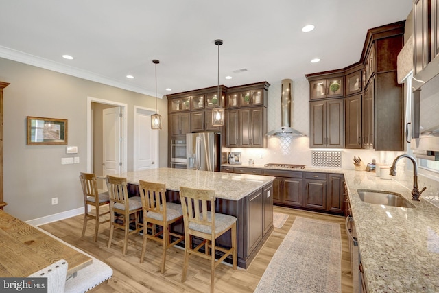 kitchen featuring wall chimney range hood, stainless steel appliances, a sink, and dark brown cabinets
