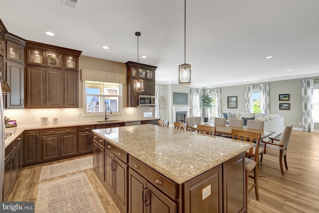 kitchen with a kitchen island, light wood-type flooring, a sink, stainless steel microwave, and recessed lighting