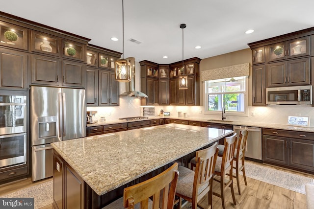 kitchen with visible vents, dark brown cabinets, a sink, stainless steel appliances, and wall chimney exhaust hood