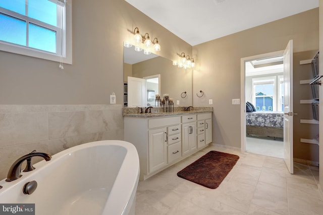 ensuite bathroom with double vanity, a wealth of natural light, a tub to relax in, and connected bathroom