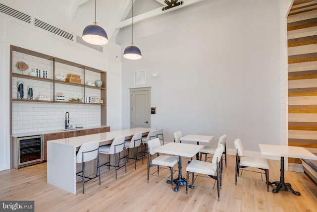 dining space with wine cooler, beamed ceiling, light wood-style floors, indoor wet bar, and high vaulted ceiling