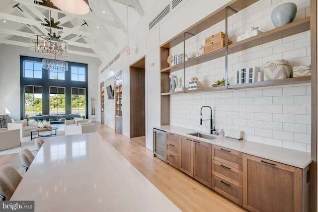 bar featuring wine cooler, beamed ceiling, high vaulted ceiling, light wood-type flooring, and a sink