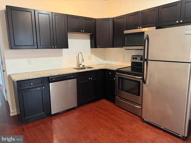 kitchen with light stone counters, dark wood finished floors, stainless steel appliances, a sink, and dark cabinets