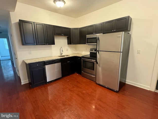 kitchen with dark cabinets, dark wood-style flooring, a sink, baseboards, and appliances with stainless steel finishes