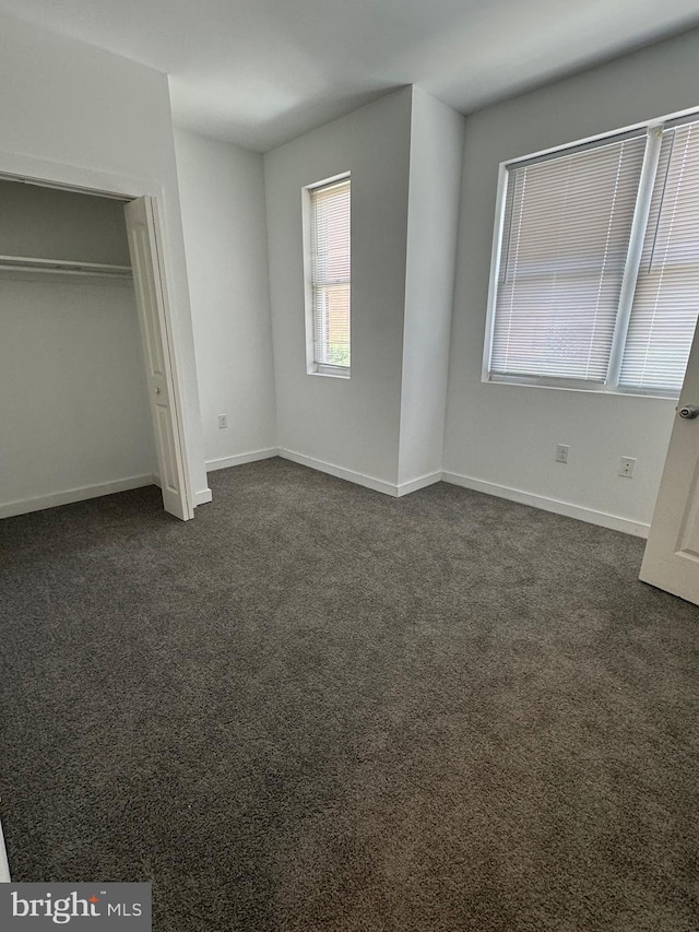 unfurnished bedroom featuring a closet, dark carpet, and baseboards