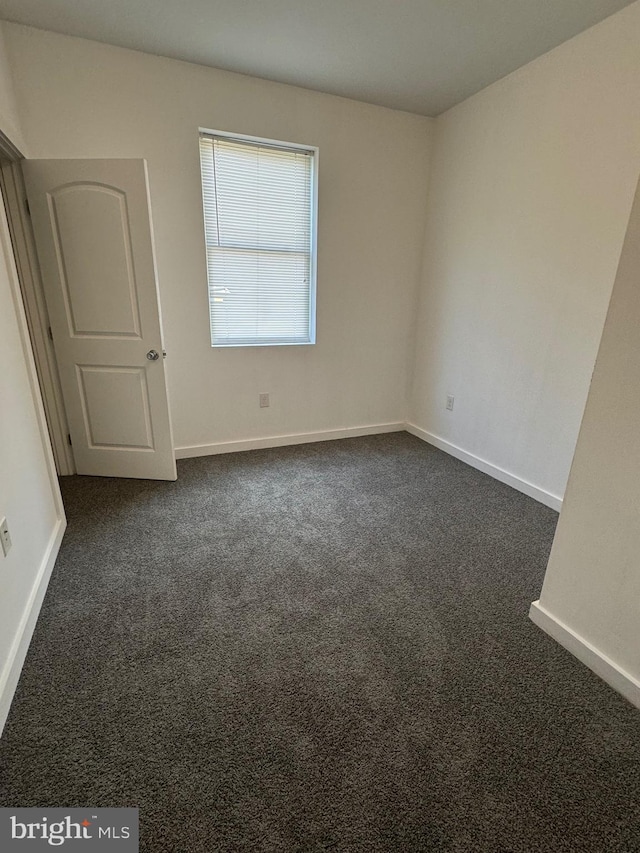 unfurnished bedroom with dark carpet and baseboards