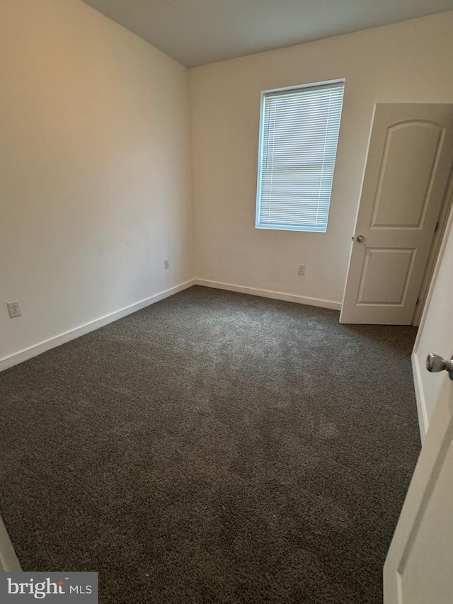 empty room featuring dark colored carpet and baseboards