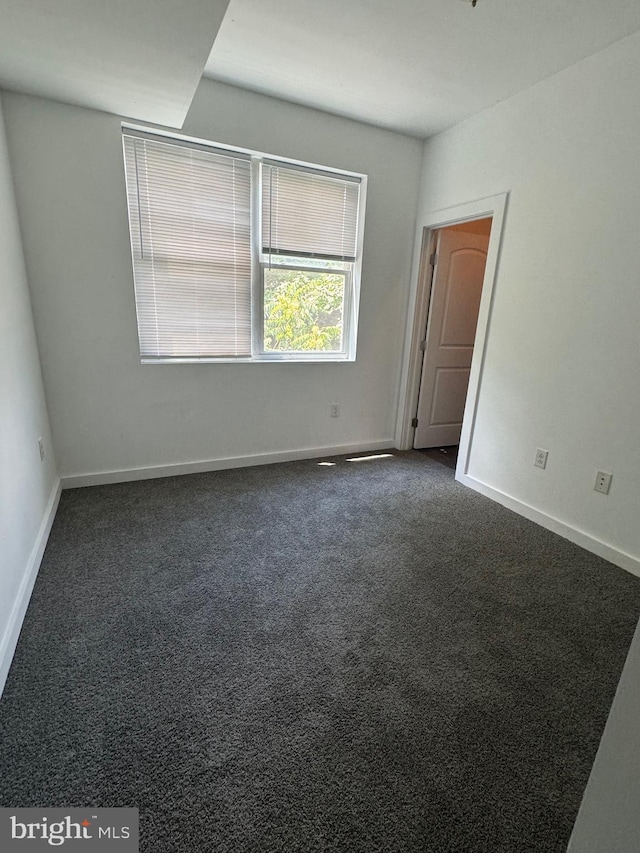 empty room with baseboards and dark colored carpet