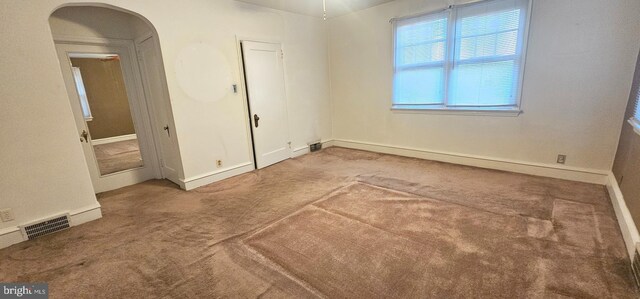 carpeted spare room with visible vents, arched walkways, and baseboards