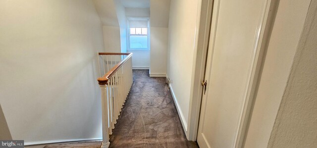 corridor featuring an upstairs landing, dark carpet, and baseboards