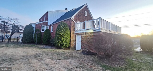 property exterior at dusk featuring brick siding, a lawn, and fence