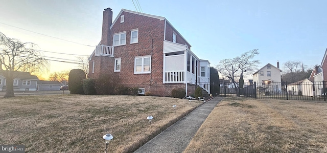 property exterior at dusk featuring brick siding, a chimney, a yard, and fence