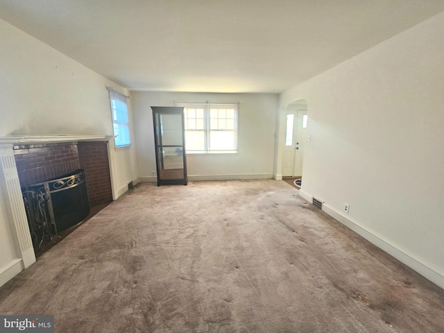 unfurnished living room with a brick fireplace, baseboards, and carpet