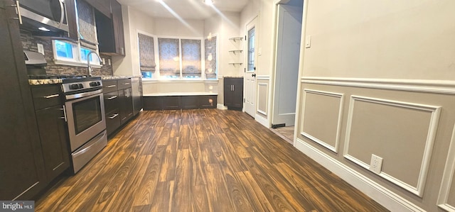 kitchen featuring dark wood-type flooring, decorative backsplash, wainscoting, appliances with stainless steel finishes, and dark cabinetry