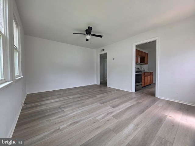 spare room featuring light wood-type flooring, ceiling fan, plenty of natural light, and baseboards