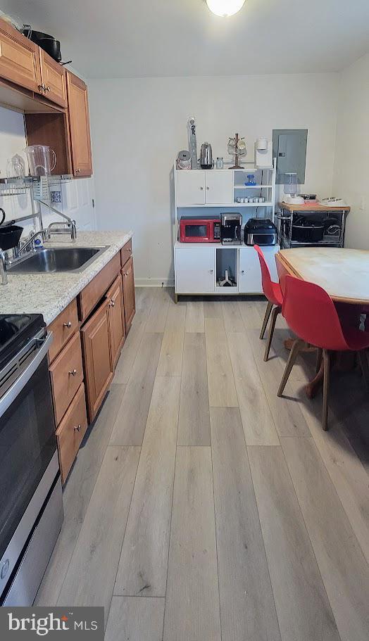 kitchen with stainless steel electric range, light wood-type flooring, brown cabinetry, and a sink