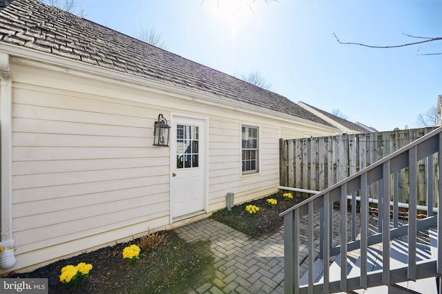 view of exterior entry with a patio area, roof with shingles, and fence