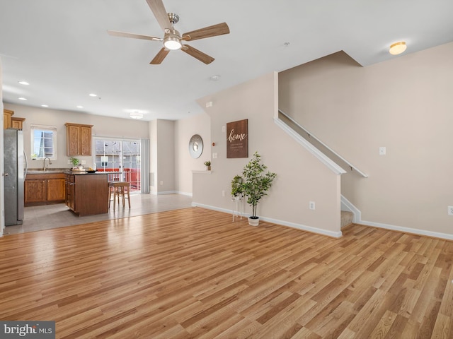 unfurnished living room with stairway, a ceiling fan, baseboards, recessed lighting, and light wood-style floors