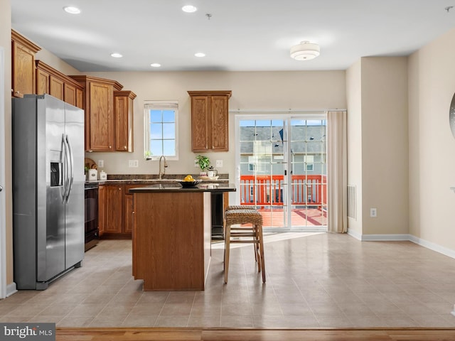 kitchen with a kitchen bar, brown cabinets, dark countertops, stainless steel fridge with ice dispenser, and range