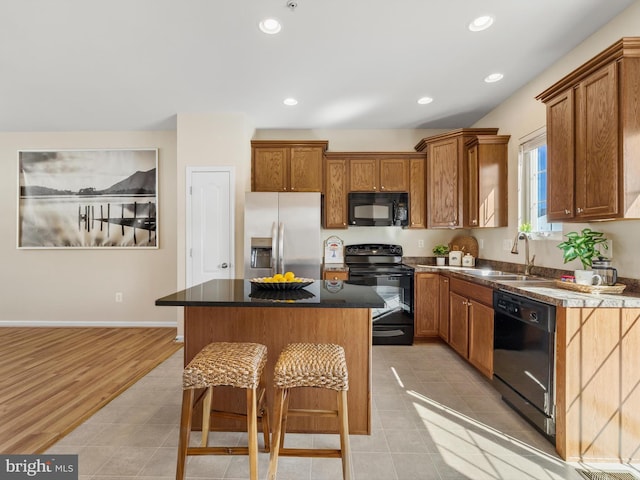 kitchen with a kitchen island, a sink, black appliances, dark countertops, and a kitchen breakfast bar