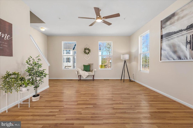 living area with light wood-type flooring, baseboards, and a ceiling fan