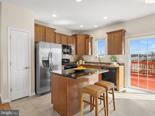 kitchen featuring a kitchen island, a kitchen bar, brown cabinetry, black appliances, and a sink