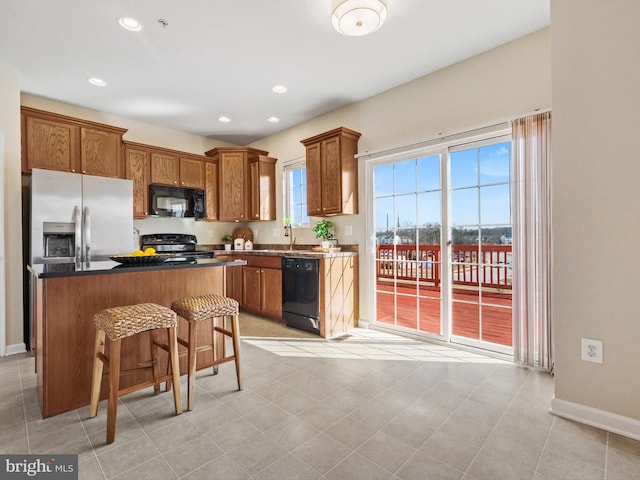 kitchen featuring brown cabinets, black appliances, a kitchen breakfast bar, dark countertops, and a kitchen island