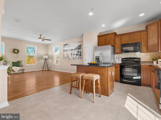 kitchen featuring black appliances, open floor plan, a center island, light tile patterned flooring, and brown cabinetry