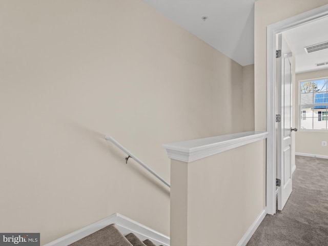 hall featuring an upstairs landing, baseboards, visible vents, and carpet floors