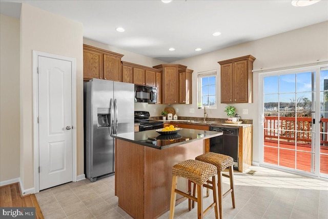 kitchen with black appliances, a breakfast bar, a sink, a center island, and brown cabinetry