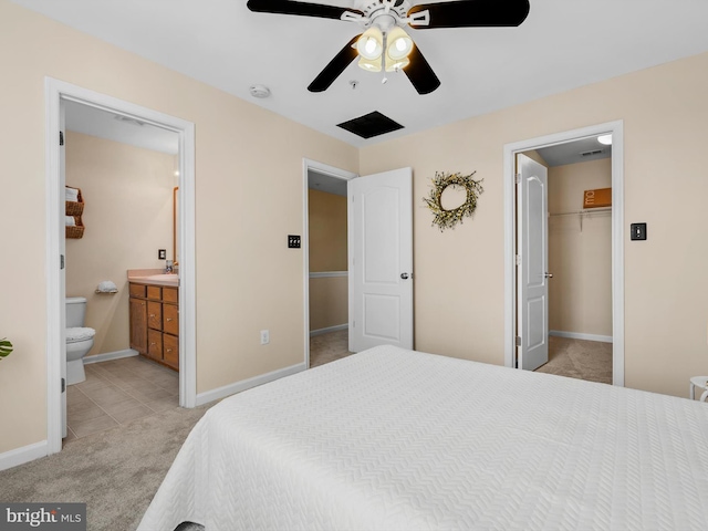 bedroom featuring baseboards, a sink, ensuite bathroom, light carpet, and a walk in closet