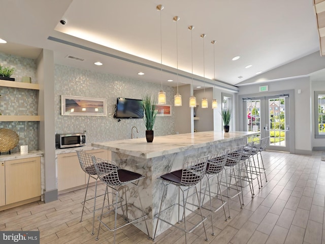 kitchen featuring wood tiled floor, a large island with sink, a kitchen bar, stainless steel microwave, and tasteful backsplash