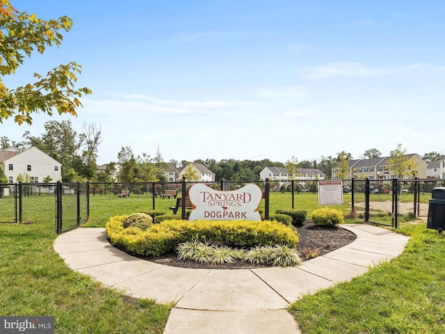 community / neighborhood sign with a gate, a yard, fence, and a residential view