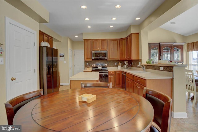 kitchen with a sink, tasteful backsplash, appliances with stainless steel finishes, a peninsula, and light countertops