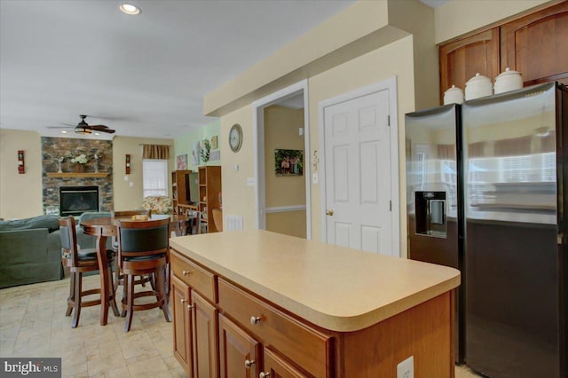 kitchen featuring a ceiling fan, a fireplace, light countertops, stainless steel fridge, and a center island