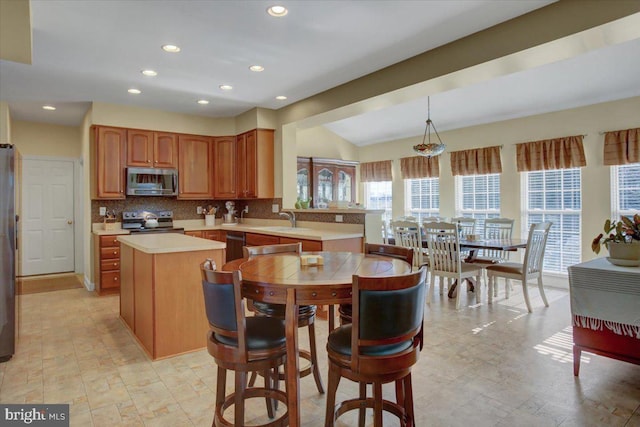 kitchen with backsplash, a center island, light countertops, appliances with stainless steel finishes, and a sink